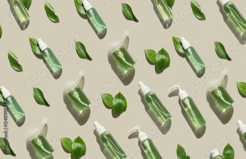 Pattern of transparent different bottles with green liquid and green leaves on beige, organic skin care, beauty and wellness, natural cosmetic products at sunlight, minimal top view, aesthetic