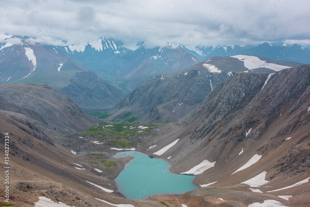 Φωτογραφία Most beautiful turquoise alpine lake in stony rocky green valley against mountain range silhouette in rainy low clouds in gray sky