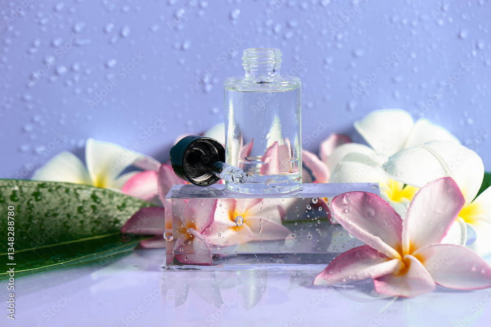 Fototapeta premium Clear serum drops rest on a glistening surface surrounded by vibrant plumeria flowers and foliage.