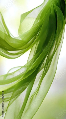A flowing green fabric drapes gracefully, capturing light and creating an ethereal feel against a soft, blurred background.