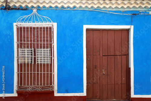 A vibrant blue building facade featuring a rustic wooden door and a window with decorative iron bars, showcasing a charming blend of bold colors and vintage architectural details. cuba .havana
