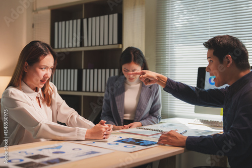 During a tense office meeting, a businessman points his finger and angrily blames his female colleagues for a mistake, creating a hostile work environment