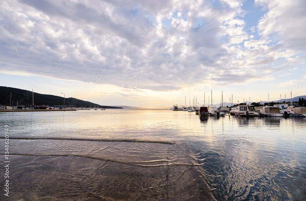 Obraz premium A tranquil harbor scene at sunset with boats docked and a cloudy sky reflecting on the calm water.