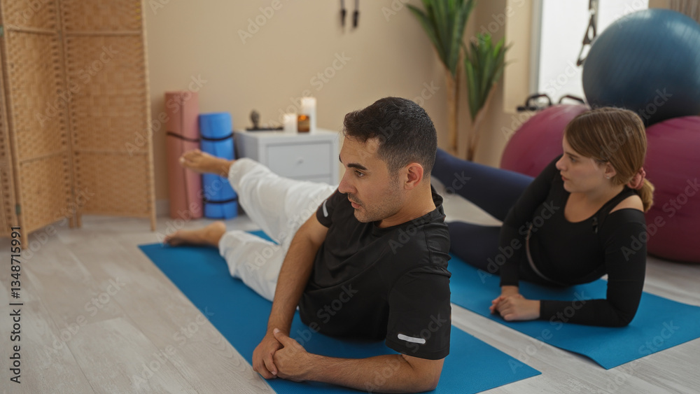 Obraz premium Man and woman practicing yoga on mats in gym with fitness equipment, emphasizing relaxation and exercise in a calm indoor environment.