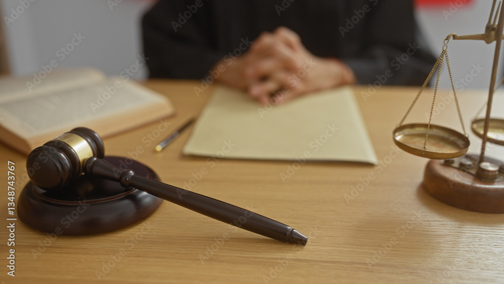 Judge sitting at desk with hands clasped, emphasis on gavel, scales, and open law book in a courtroom setting Judge sitting at desk with hands clasped, emphasis on gavel, scales, and open law book in a courtroom setting