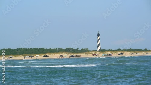 Cape Hatteras lighthouse of North Carolina with the ocean and beach lined with parked trucks and tourists.