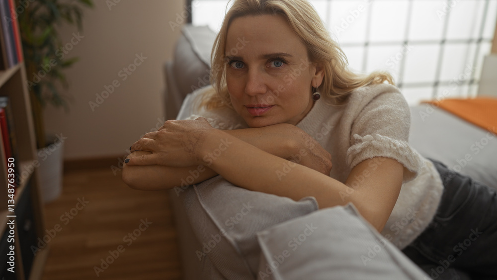 Woman relaxing at home with a serene expression, this blonde, mature female lounges comfortably on a sofa in a cozy living room setting with soft lighting. Woman relaxing at home with a serene expression, this blonde, mature female lounges comfortably on a sofa in a cozy living room setting with soft lighting.