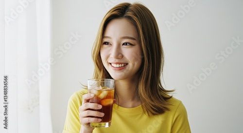A young woman in yellow, joyfully holding a transparent glass with a bubbly drink, smiling widely.
