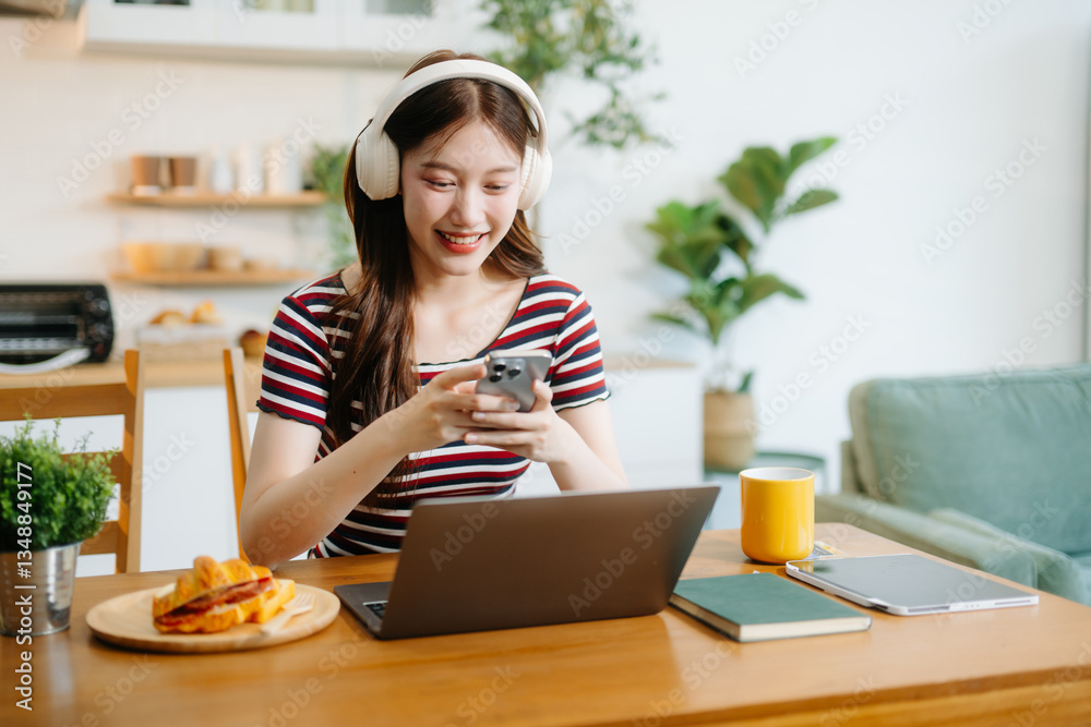 Happy woman with headphones working on a tablet in a bright kitchen. Ideal for themes of remote work Happy woman with headphones working on a tablet in a bright kitchen. Ideal for themes of remote work