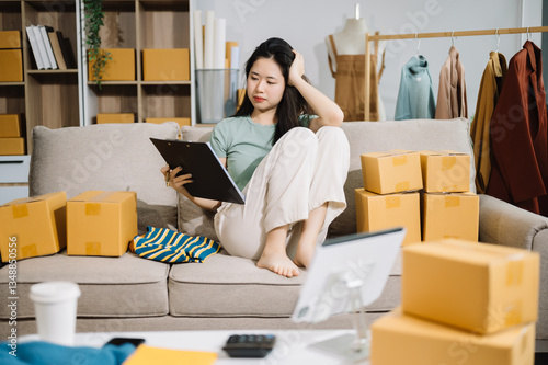 Asian owner woman prepare parcel box  woman is stressed, bored, and overthinking from working and standing check online orders for deliver to customer. photo