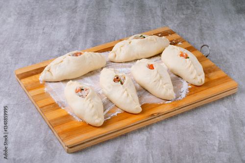 Raw rasstegai made from yeast dough with fish filling on a wooden board with flour. Preparation for baking, proofing of pies. Step by step