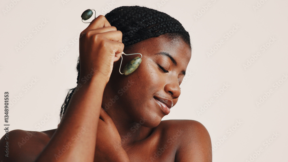 Fototapeta premium Facial roller, beauty and black woman in studio with natural, health and skincare routine. Wellness, massage and African female person with jade stone tool for lymphatic drainage by white background.