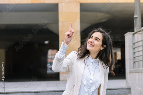 Confident businesswoman pointing up with a smile outdoors. Lifestyle, business. photo