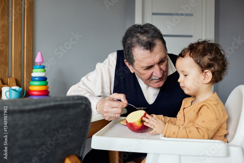Grandfather and grandson are enjoying apple slices together while laughing in a cozy dining area