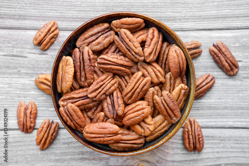 Photograph of dried pecan nuts without shell in a bowl on wooden background. Top view. Healthy eating and snack, whole foods. Natural fats, fibre, minerals, vitamins.