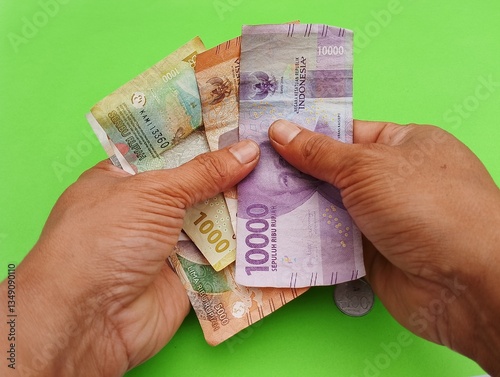 Asian Man Hand Counting Indonesian Money - Rupiah with variety denomination isolated on green background.