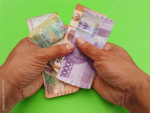 Asian Man Hand Counting Indonesian Money - Rupiah with variety denomination isolated on green background.