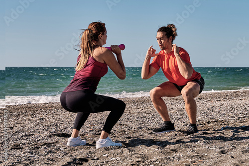 Personal trainers performing squats on the beach at sea during summer vacation