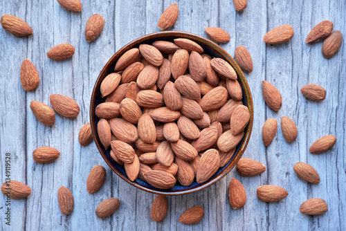 Photograph of dried almonds nuts in a bowl on wooden background. Top view.  Healthy eating and snack, whole foods. Source of protein and magnesium.