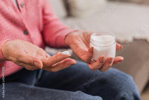 Obraz na plátně Senior woman in 60s nourishing hand cream to skin, taking care of hands