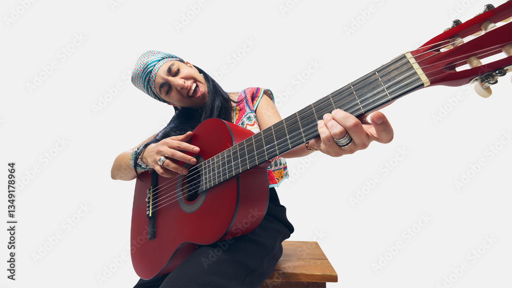Obraz premium Low-angle close-up of female guitarist in colorful outfit, playfully leaning forward while strumming red guitar. Concept of music, passion, rhythm, festival, joy, artistic movement, performance energy