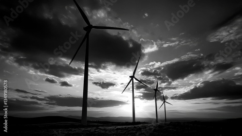 Power in Motion: Silhouetted wind turbines stand tall against a dramatic, cloudy sky in this black and white image, representing sustainable energy.