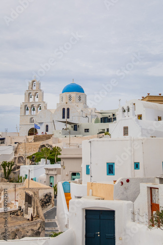 Fototapeta Naklejka Na Ścianę i Meble -  Pyrgos Kallistis, central hilltop village in Santorini, Greece. Vertical view of Saint George Church in historic Greek town with cloudy sky, whitewashed homes, blue domes and traditional architecture