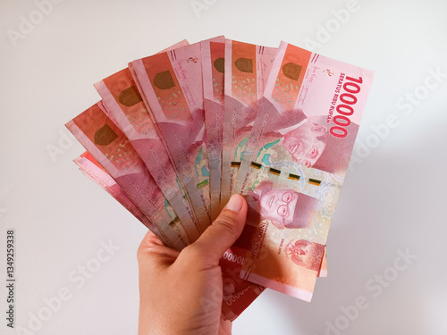 Woman's hand holding one hundred thousand rupiah banknote Indonesian currency isolated on white background.