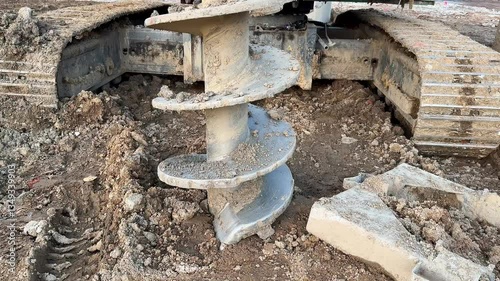 Close-up view of a drilling auger attached to heavy machinery, showing earth excavation in progress.