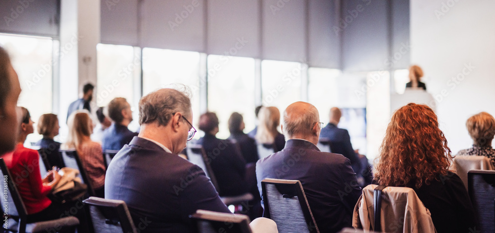 Obraz premium Business and entrepreneurship symposium. Female speaker giving a talk at business meeting. Audience in conference hall. Rear view of unrecognized participant in audience.