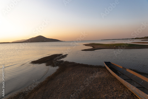 Pa Sak Jolasid Dam, Serene Coastal Sunset: A tranquil view of an island at dusk, with a silhouette of hills and serene water reflecting the warm colors of the setting sun, creating a peaceful
