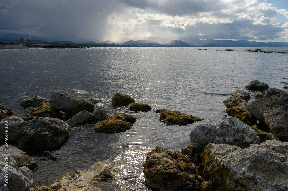 Sunlight glimmers on water as waves lap against rocky shore at tranquil seascape Sunlight glimmers on water as waves lap against rocky shore at tranquil seascape