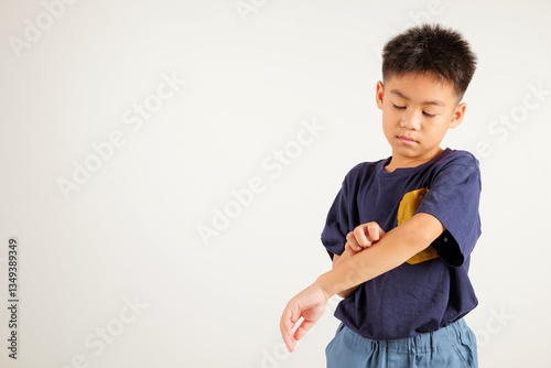 Asian little kid boy scratching itchy arm from a mosquito bite at studio shot isolated on white background, Portrait of Thai primary child dermatitis and scabies, Allergy symptoms, Malaria day concept