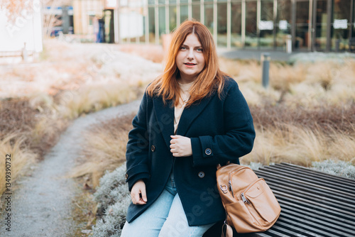 Obraz na płótnie Happy woman sitting on the bench outdoors. Urban, people concept. Smiling 30s redhead woman posing at sunny day on the city street, spring time w salonie