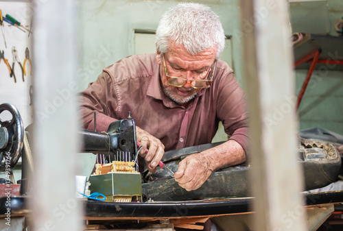 Принти на полотні A colombian upholsterer repairing a leather cushion with pliers inside a workshop in Yaguará, Huila, Colombia