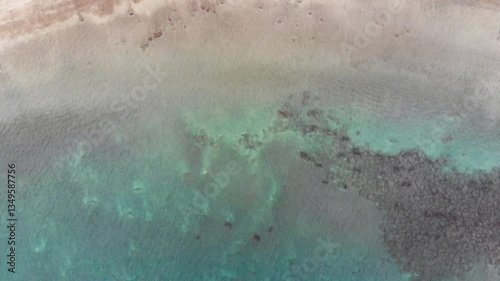 Aerial view of ocean shore, sandy beach. Beautiful clear turquoise calm water on coastline, black and yellow sand shuffled in coastal tide, sand ripples, natural textures. 4K drone video, birds-eye