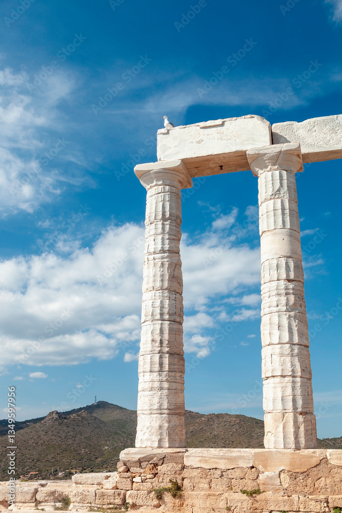 Seagull spreading wings on an ancient marble ruin at the Temple of Poseidon, Sounion, Greece, highlighting bright blue sky and classical architecture