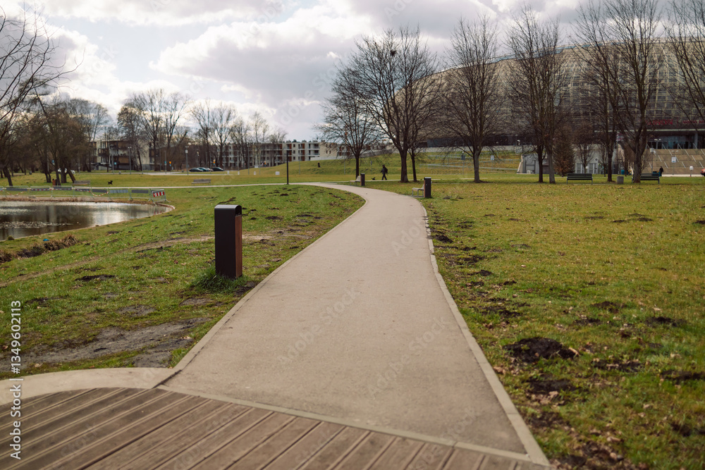 A serene view of a walking path in a park, surrounded by grass, trees, and open space. The peaceful scene highlights nature and outdoor leisure activities, ideal for walking and relaxation