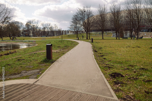 Obraz na płótnie A serene view of a walking path in a park, surrounded by grass, trees, and open space. The peaceful scene highlights nature and outdoor leisure activities, ideal for walking and relaxation w salonie