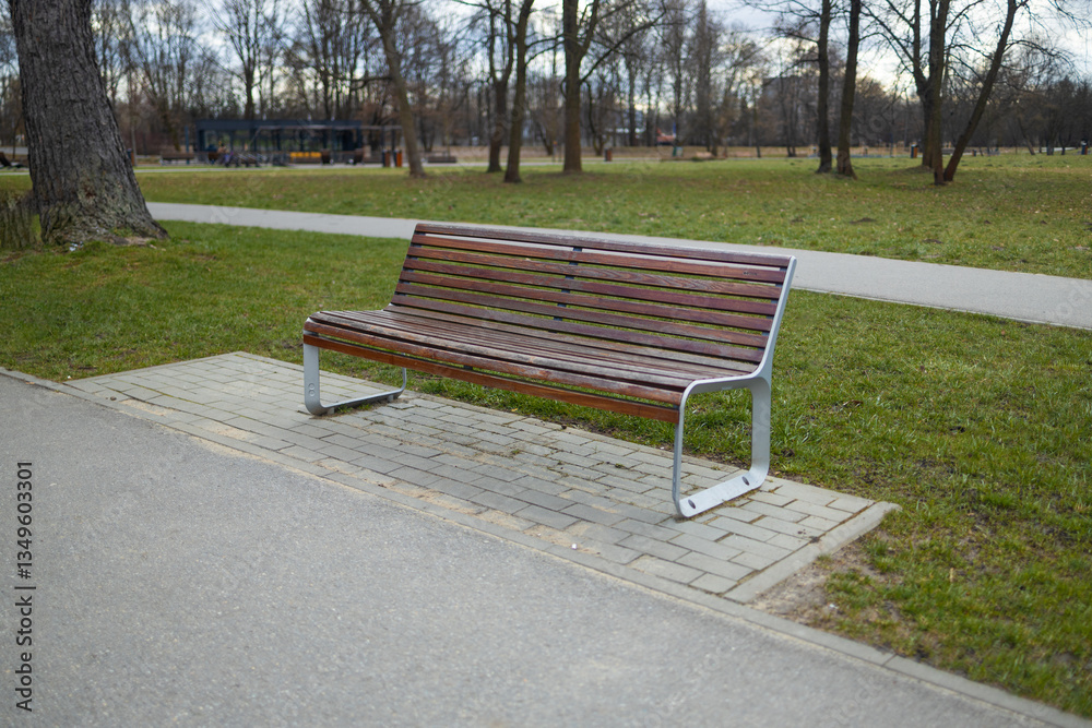A peaceful park scene featuring a wooden bench along a walking path. The bench provides a place to relax while enjoying the view of the surrounding trees and greenery in a public park