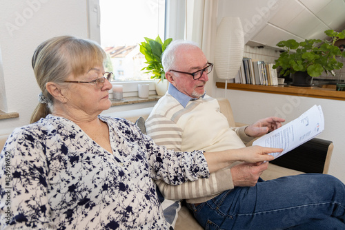 senior couple sit with paper document. Unhappy older mature man woman reading paper bill managing bank finances calculating taxes planning loan debt pension payment