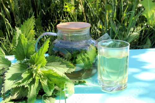 A decoction of nettle leaves in a teapot stands on a wooden table.