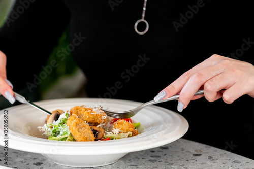 Wallpaper Mural A fresh salad with breaded chicken, mushrooms, grated cheese, served in a white bowl. A person with a fork and knife prepares to eat. Close-up on a speckled countertop. Torontodigital.ca