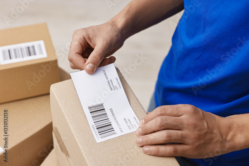 Man sticking shipping label with barcode on parcel indoors, closeup photo
