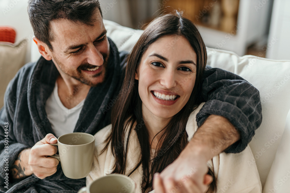 Happy couple cuddling on sofa, drinking coffee and enjoying their time together Happy couple cuddling on sofa, drinking coffee and enjoying their time together