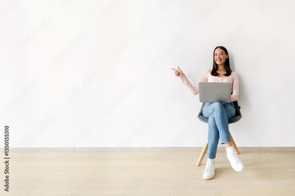 Happy freelance lady sitting in chair and using laptop, pointing aside at copy space over white wall, woman working or trading online Happy freelance lady sitting in chair and using laptop, pointing aside at copy space over white wall, woman working or trading online