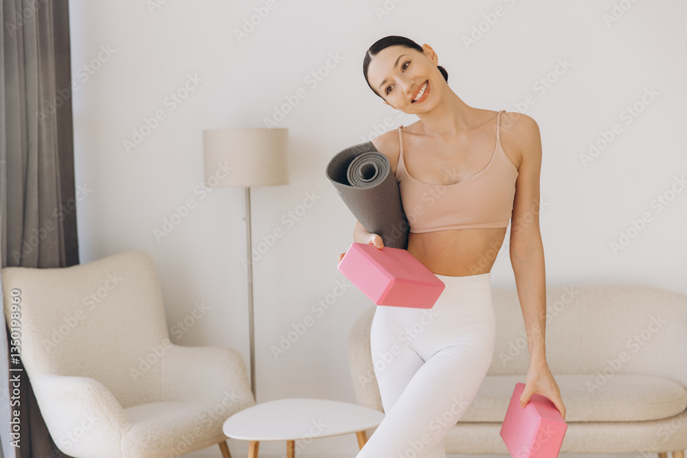 Young woman holding yoga mat and blocks, getting ready for home workout Young woman holding yoga mat and blocks, getting ready for home workout
