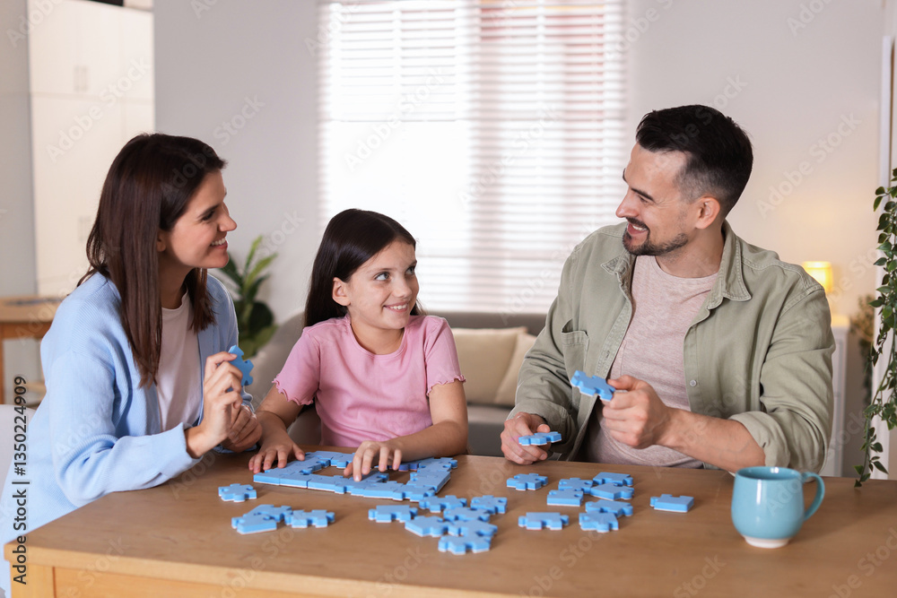 Fototapeta premium Happy parents and their daughter solving puzzle together at wooden table indoors