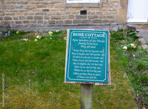 Eham, Chesterfield, United Kingdom - 21 Mar 2025 - A green sign with a poem on it is placed in a grassy area. Passing of members from the black death. The sign is surrounded by flowers, which adds to 