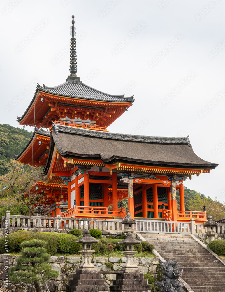 Kiyomizudera's Pagoda Sanjunodo and Nishimon Gate in Kyoto, Japan. A three-tiered vermilion pagoda with gray tiled roofs and ornate spire stands elevated on stone foundations amid manicured gardens. Kiyomizudera's Pagoda Sanjunodo and Nishimon Gate in Kyoto, Japan. A three-tiered vermilion pagoda with gray tiled roofs and ornate spire stands elevated on stone foundations amid manicured gardens.